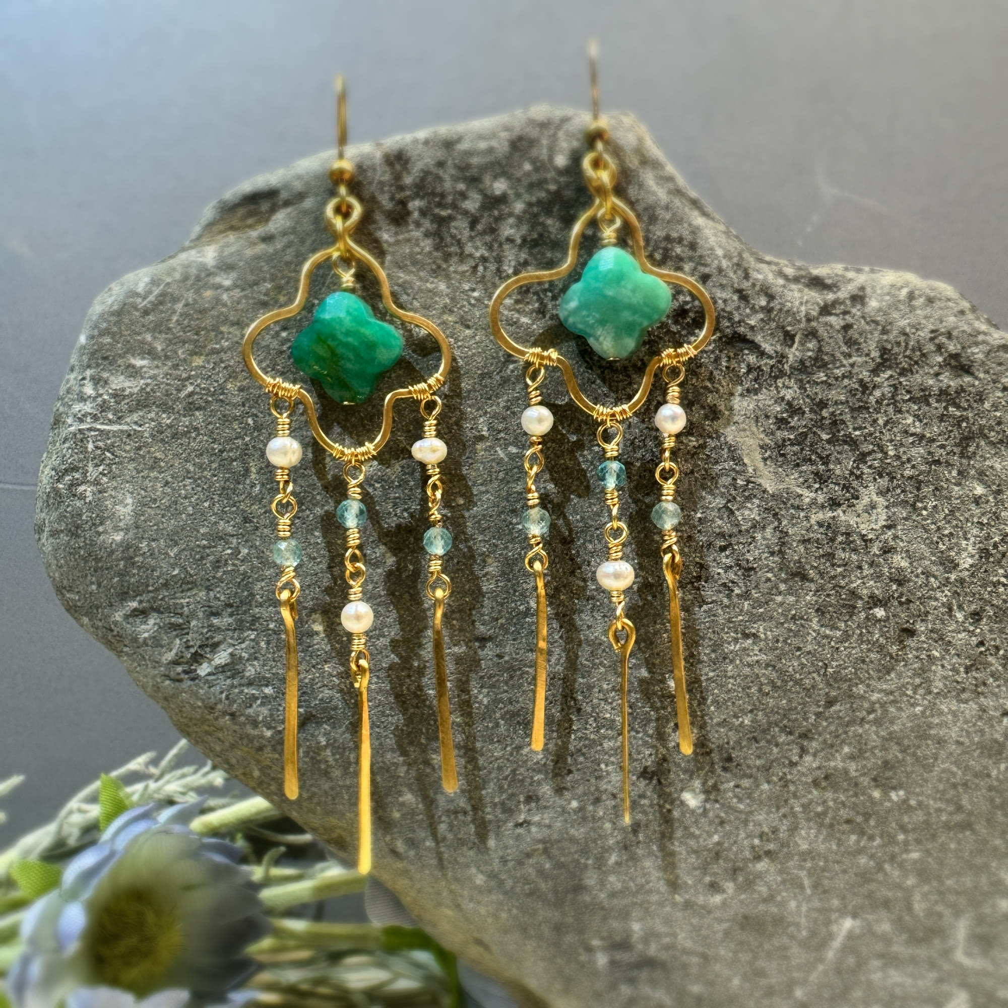 Gold clover green stone pearl tassel earrings displayed on natural stone